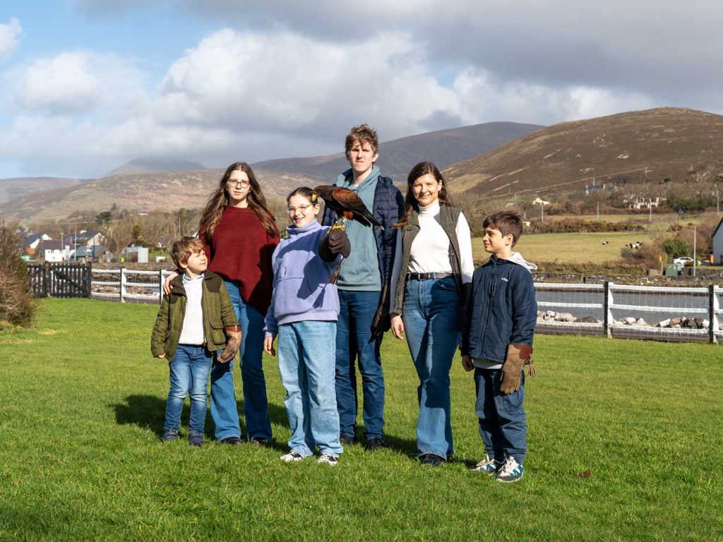 A falcon sitting on a gloved hand with a family posing in the background