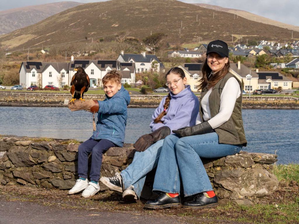 A group of happy people sitting near the water with a falcon perched on their arm